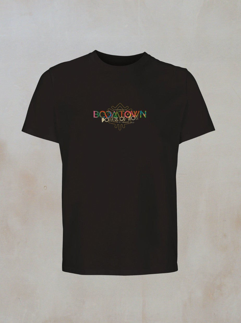 The Power of Now: Graphic T-Shirt from Boomtown Fair Shop features a colorful abstract design and BOOMTOWN and POWER OF NOW on the chest, displayed in black organic cotton against a light beige background.