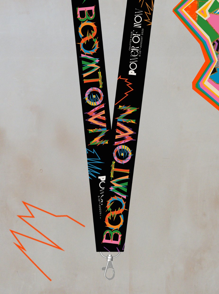 The Chapter Four: Power of Now Lanyard by Boomtown Fair Shop features bold, colorful zigzag patterns and a metal clasp. Shown on a light background with orange and multicolored shapes, its perfect as a festival accessory for onsite collection.