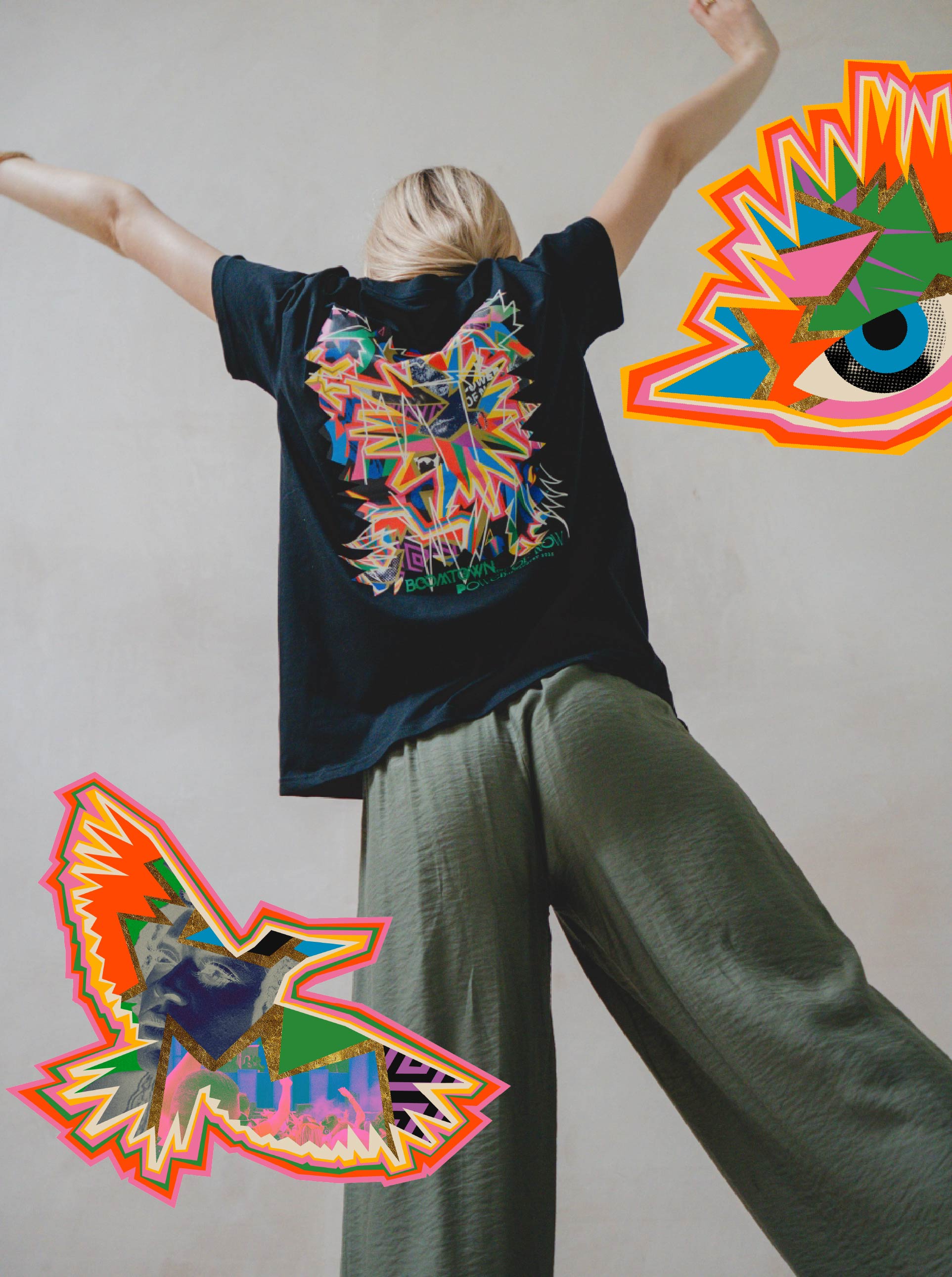 A person stands with arms raised, wearing the Boomtown Fair Shop’s Chapter Four: Power of Now Graphic T-Shirt in black organic cotton. The plain backdrop features two bold stickers—an abstract bird and eye—evoking the signature Boomtown vibe.