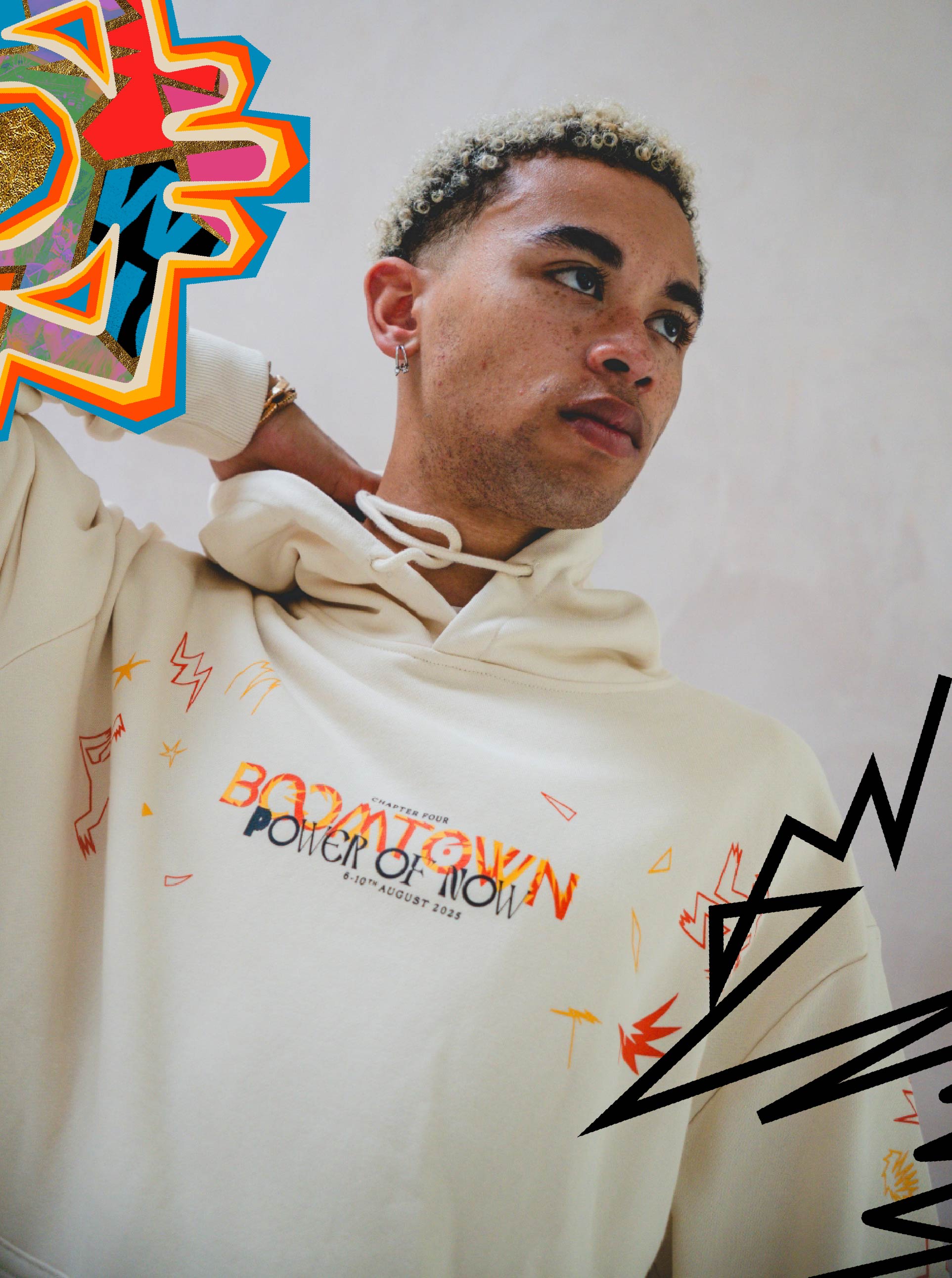 A person with short curly hair wears the Boomtown Fair Shop’s Power of Now: Limited Edition Emberkind Hoodie in cream, made from organic soft cotton and featuring colorful abstract graphics and bold, energetic surrounding shapes.
