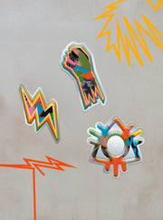 The Pin Badge Set from Boomtown Fair Shop features a raised fist, an orange zigzag lightning bolt, and a round badge with multicolored drips—perfect festival gear to capture the Boomtown spirit. Orange zigzag corners add a bold finishing touch.