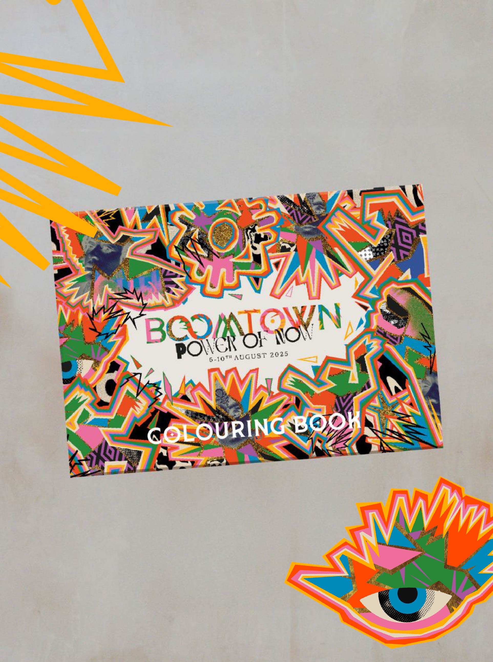 The Boomtown Fair Shop Colouring Book is featured against a gray background with orange shapes and a vibrant eye graphic, showcasing Boomtown-inspired artwork and iconic festival scenes.
